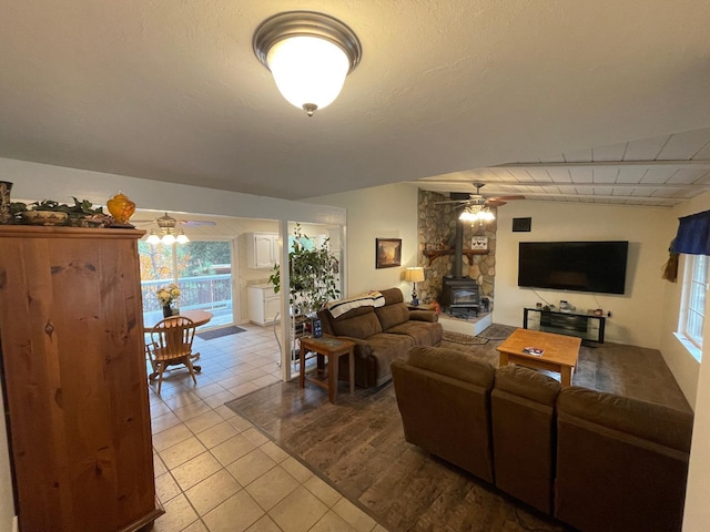 living room featuring light tile patterned floors, ceiling fan, and a wood stove