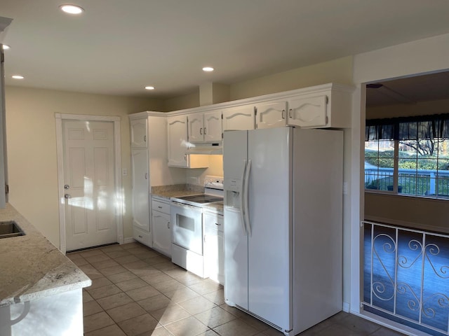 kitchen with white appliances, white cabinetry, light stone countertops, and light tile patterned floors