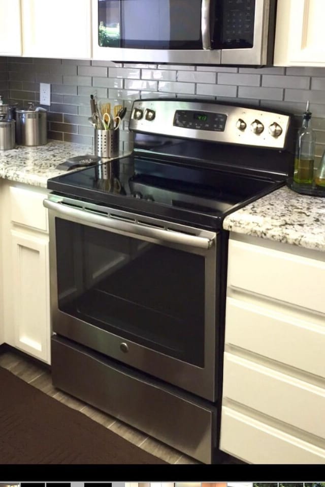 kitchen featuring decorative backsplash, stainless steel appliances, white cabinets, and light stone countertops