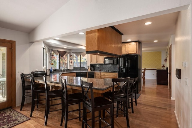 kitchen with a breakfast bar, dark stone counters, kitchen peninsula, tasteful backsplash, and wood-type flooring