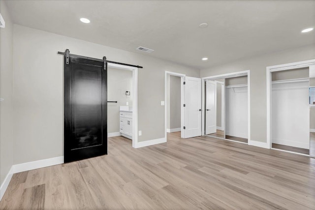 unfurnished bedroom with a barn door, multiple closets, connected bathroom, and light hardwood / wood-style flooring