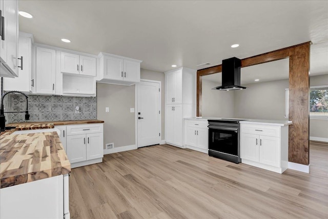 kitchen with light wood-type flooring, exhaust hood, black range, butcher block countertops, and white cabinetry