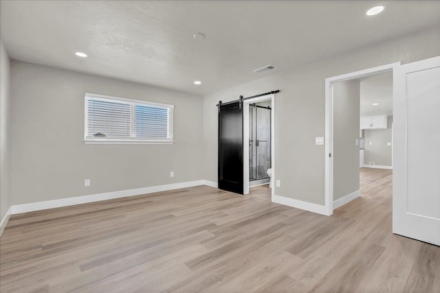 unfurnished bedroom with a barn door and light hardwood / wood-style flooring