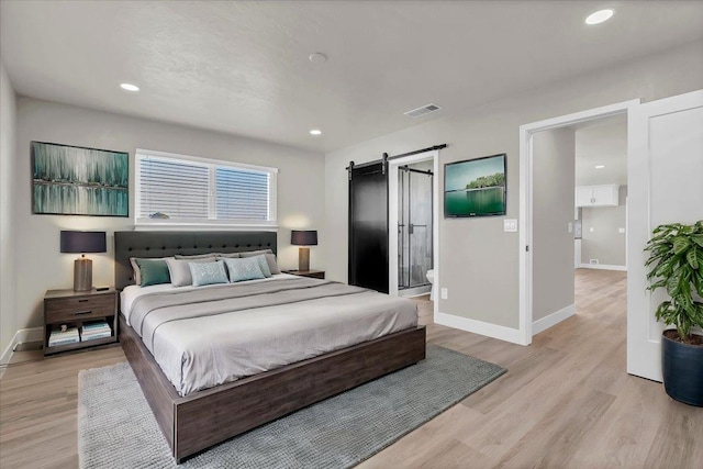 bedroom featuring a barn door, light hardwood / wood-style flooring, and connected bathroom