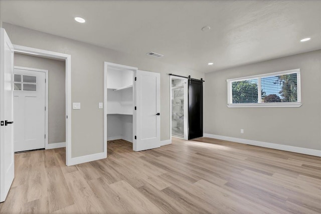 unfurnished bedroom with ensuite bathroom, a walk in closet, light hardwood / wood-style flooring, a barn door, and a closet