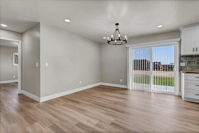 unfurnished dining area with a notable chandelier and light wood-type flooring