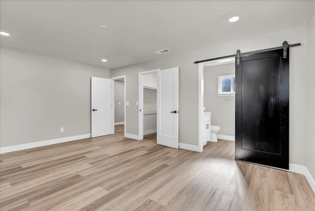 unfurnished bedroom featuring a barn door, a spacious closet, light hardwood / wood-style flooring, and ensuite bath