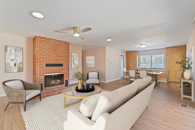 living room with a brick fireplace, ceiling fan, and light wood-type flooring