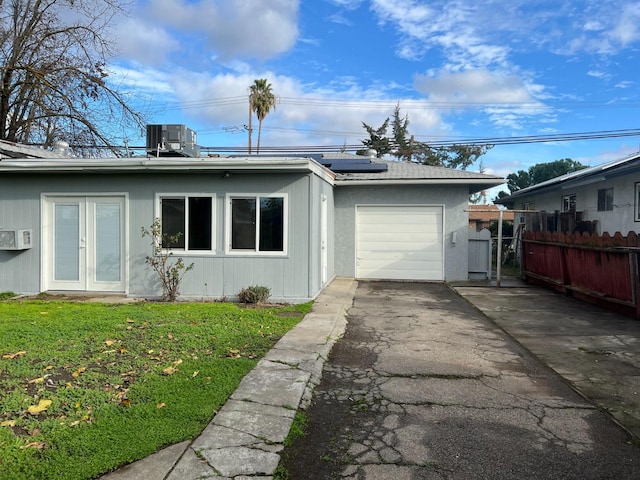 view of front of property featuring french doors, a garage, central air condition unit, solar panels, and a front lawn