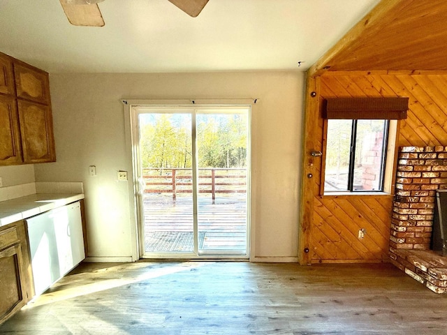 interior space featuring ceiling fan, a brick fireplace, light hardwood / wood-style flooring, and wooden walls