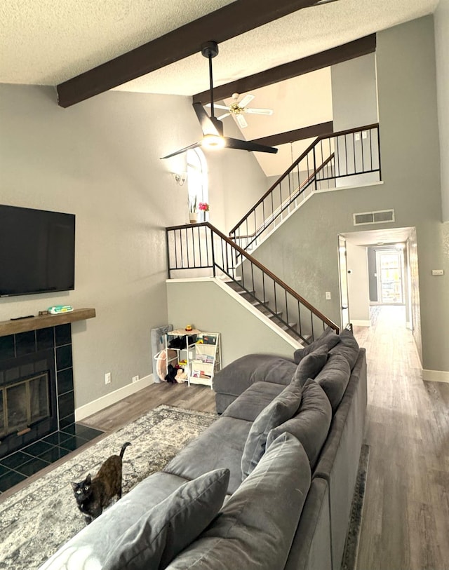 living room with hardwood / wood-style floors, ceiling fan, a fireplace, a textured ceiling, and beam ceiling