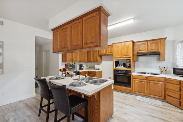 kitchen with white gas cooktop, a kitchen breakfast bar, sink, light hardwood / wood-style flooring, and black oven