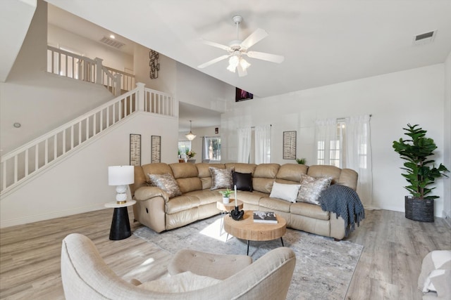 living room with plenty of natural light, ceiling fan, light wood-type flooring, and a high ceiling