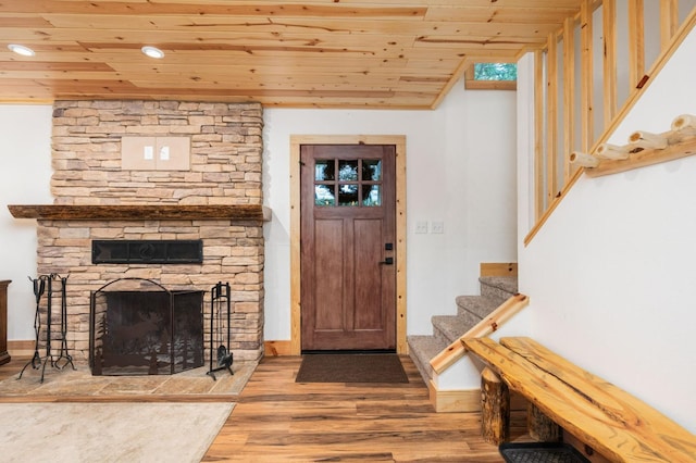 entrance foyer featuring wood finished floors, wooden ceiling, stairway, and a stone fireplace