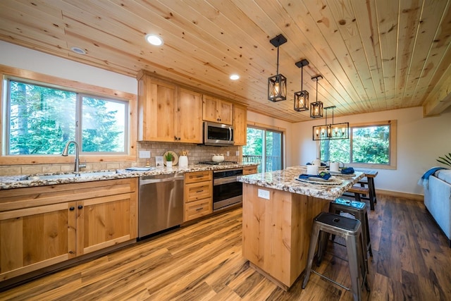 kitchen with a sink, appliances with stainless steel finishes, light wood-type flooring, decorative backsplash, and a center island