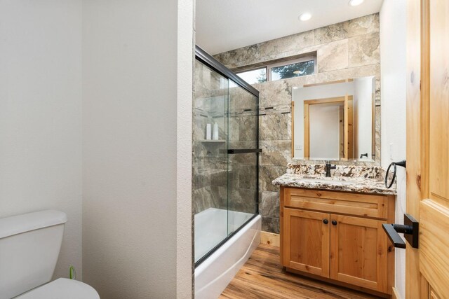 full bath with toilet, bath / shower combo with glass door, wood finished floors, and vanity