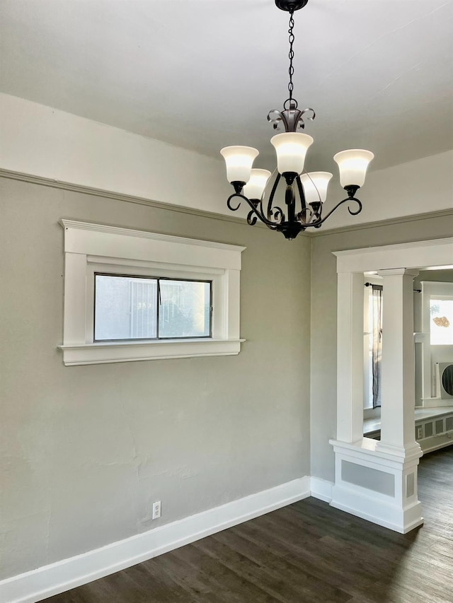 spare room with ornate columns, dark wood-type flooring, and a notable chandelier