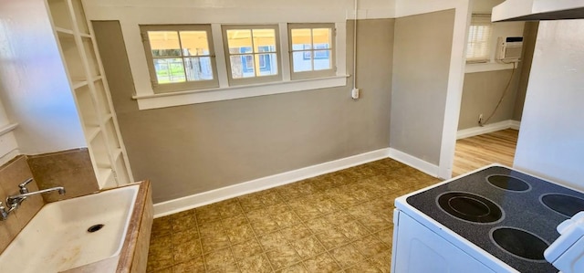 kitchen with electric range oven, a wall unit AC, a healthy amount of sunlight, and sink