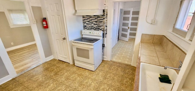 kitchen featuring a wealth of natural light, electric range, decorative backsplash, and ventilation hood