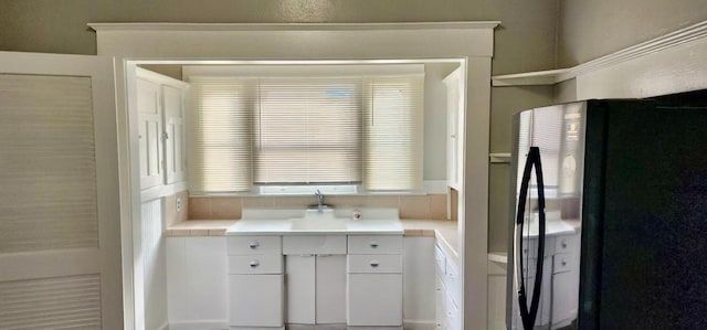 kitchen featuring white cabinetry, black fridge, and sink