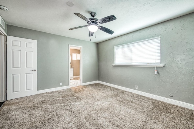 unfurnished bedroom with ceiling fan, ensuite bathroom, carpet flooring, and a textured ceiling