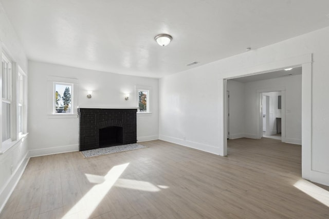 unfurnished living room featuring light hardwood / wood-style floors, a wealth of natural light, and a brick fireplace