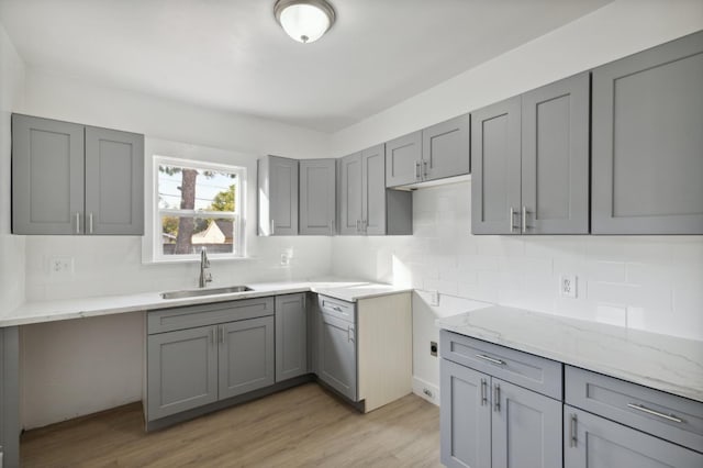 kitchen featuring light wood-type flooring, gray cabinets, backsplash, and sink