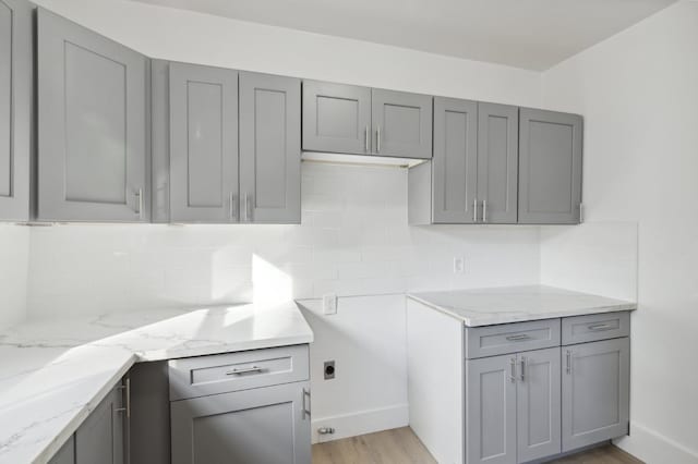 kitchen with light hardwood / wood-style floors, gray cabinets, tasteful backsplash, and light stone counters