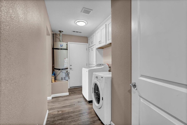 clothes washing area with cabinets, washing machine and dryer, light wood-type flooring, a textured ceiling, and water heater