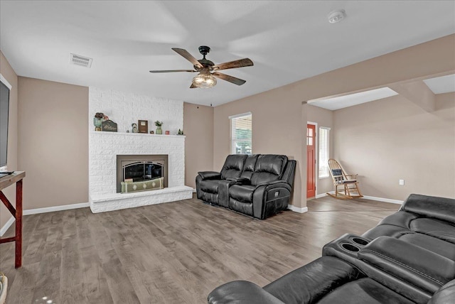 living room featuring ceiling fan, a fireplace, and wood-type flooring