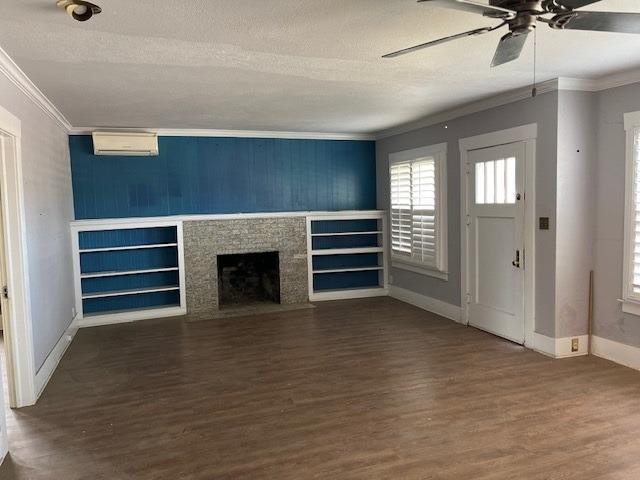 unfurnished living room with a fireplace, a textured ceiling, an AC wall unit, and crown molding