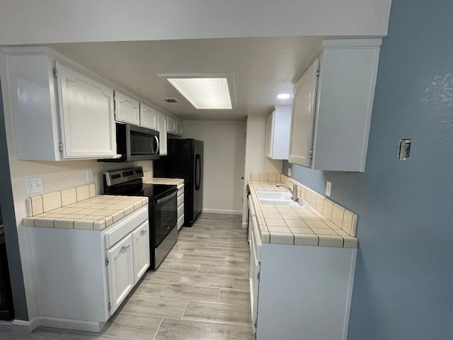 kitchen featuring tile countertops, sink, white cabinetry, and stainless steel appliances