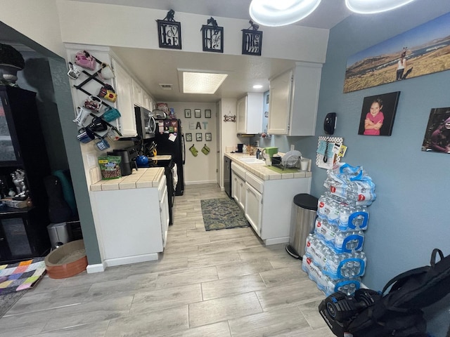 kitchen featuring tile countertops, white cabinetry, black appliances, and sink