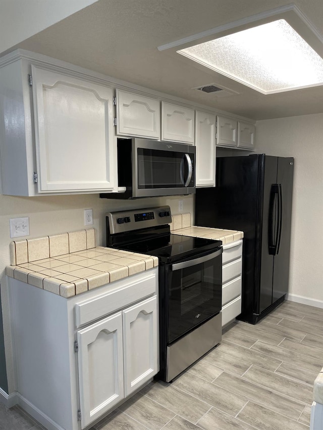 kitchen with light wood-type flooring, stainless steel appliances, white cabinetry, and tile counters