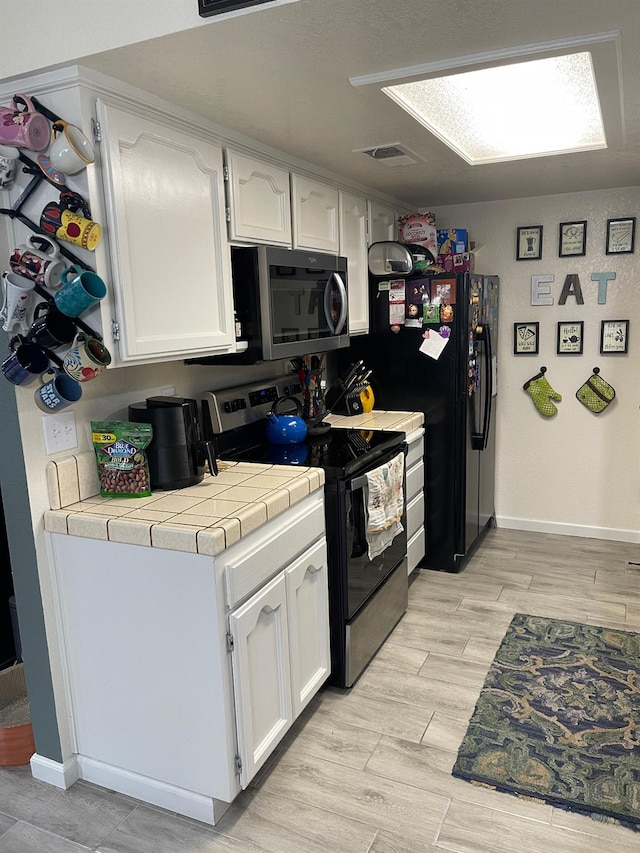 kitchen with white cabinetry, tile counters, stainless steel appliances, and light wood-type flooring