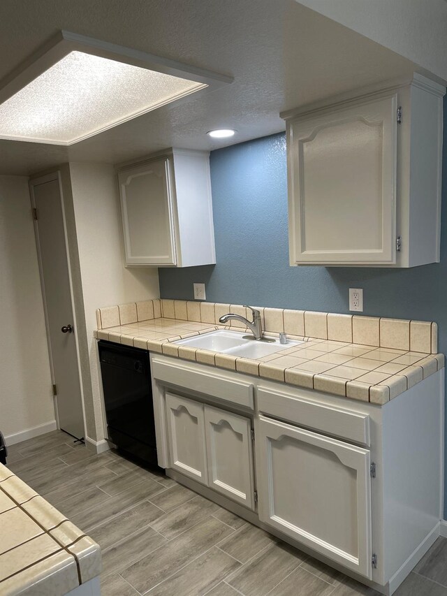 kitchen featuring white cabinets, sink, light wood-type flooring, black dishwasher, and tile counters