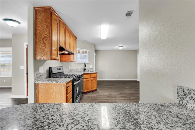 kitchen featuring dark hardwood / wood-style floors, light stone counters, a wealth of natural light, and stainless steel gas range