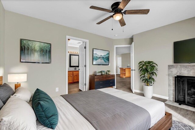 bedroom with a high end fireplace, ensuite bathroom, ceiling fan, sink, and dark hardwood / wood-style floors