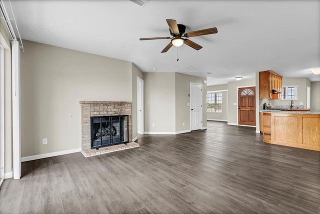 unfurnished living room with ceiling fan, sink, dark wood-type flooring, and a brick fireplace