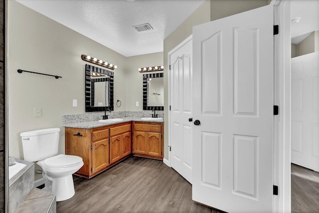 bathroom with vanity, toilet, wood-type flooring, and a textured ceiling