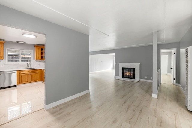 unfurnished living room featuring a brick fireplace, sink, and light hardwood / wood-style flooring