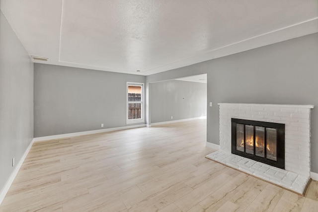 unfurnished living room with light hardwood / wood-style floors, a brick fireplace, and a textured ceiling