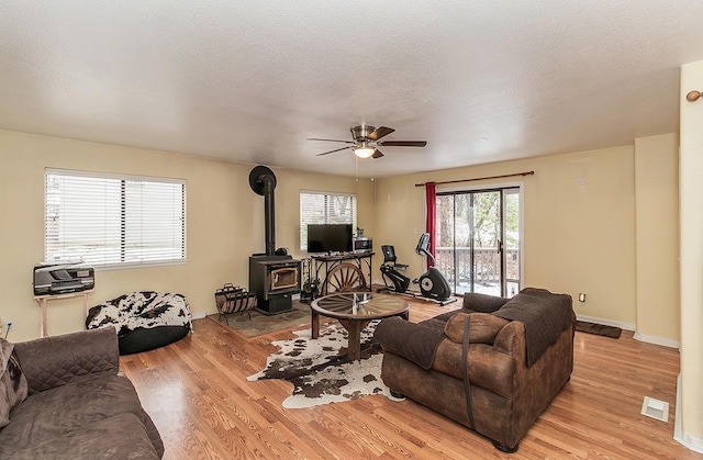 living room featuring a wood stove, light wood-style floors, visible vents, and a textured ceiling