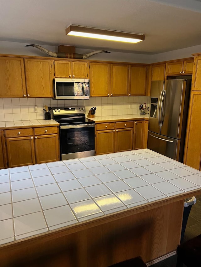 kitchen featuring brown cabinets, tile counters, stainless steel appliances, and backsplash