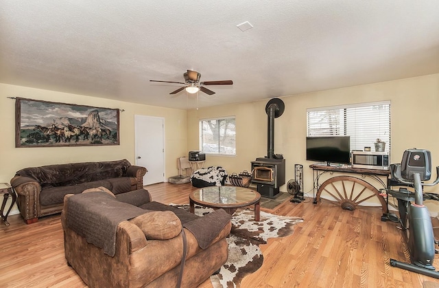 living room featuring a wood stove, light wood-style flooring, and a textured ceiling