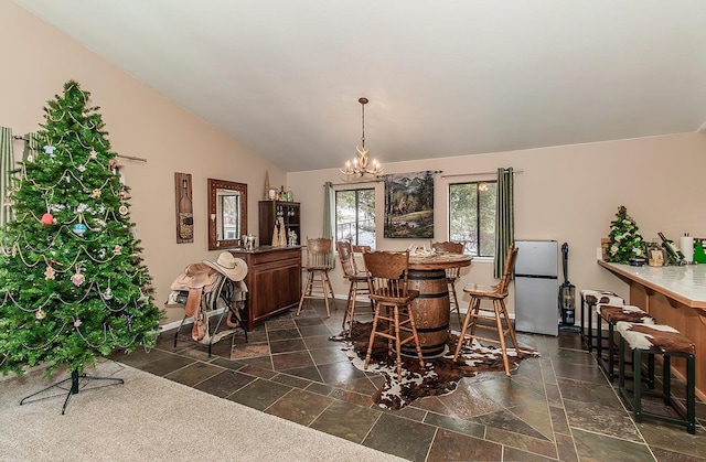 dining space with baseboards, a chandelier, vaulted ceiling, and stone tile flooring