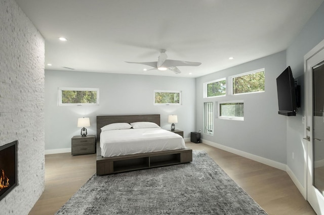 bedroom featuring light wood-type flooring, a stone fireplace, and ceiling fan