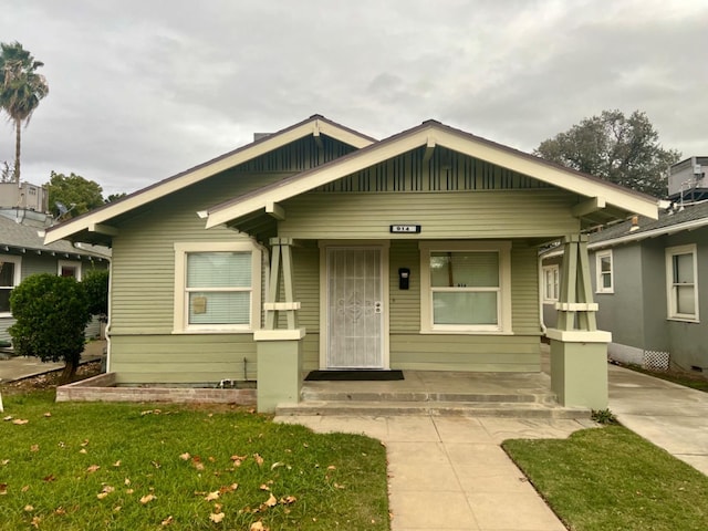 bungalow-style house featuring covered porch, a front yard, and central AC