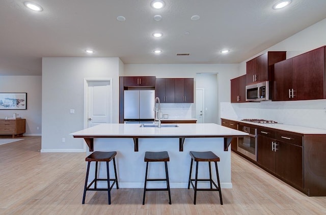 kitchen with appliances with stainless steel finishes, light wood-type flooring, a kitchen breakfast bar, sink, and a center island with sink