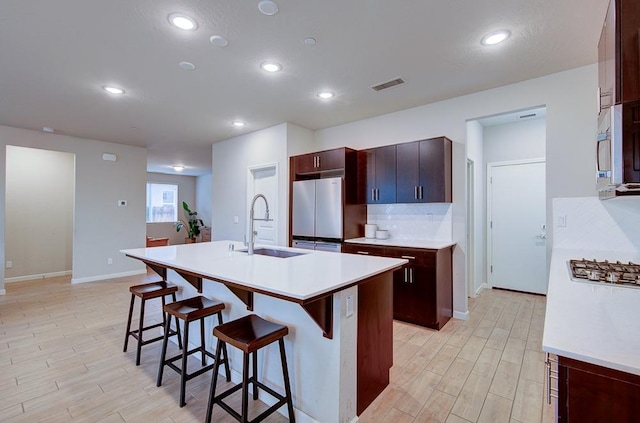 kitchen featuring a breakfast bar, white refrigerator, sink, an island with sink, and light hardwood / wood-style floors